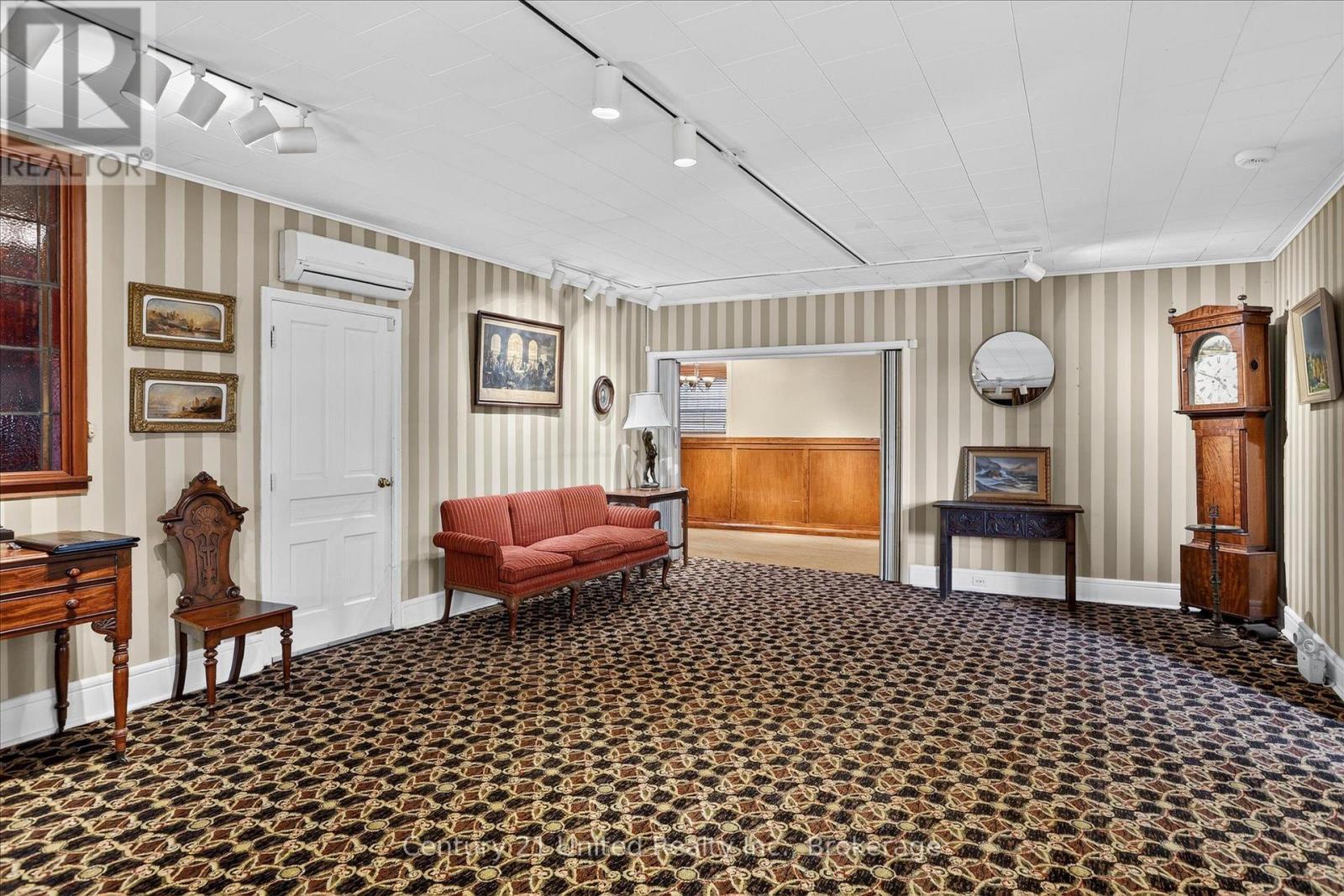 Furnished room with striped walls, patterned carpet, a red sofa, and an antique grandfather clock.