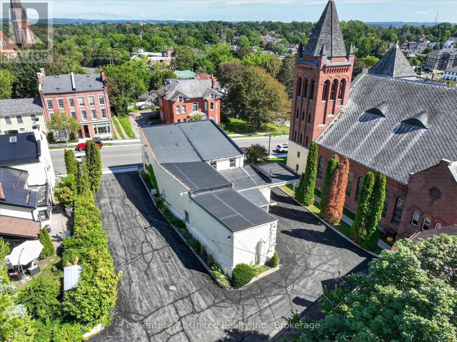 Aerial view of a white commercial building and paved lot beside a red-brick church with a tall steeple.