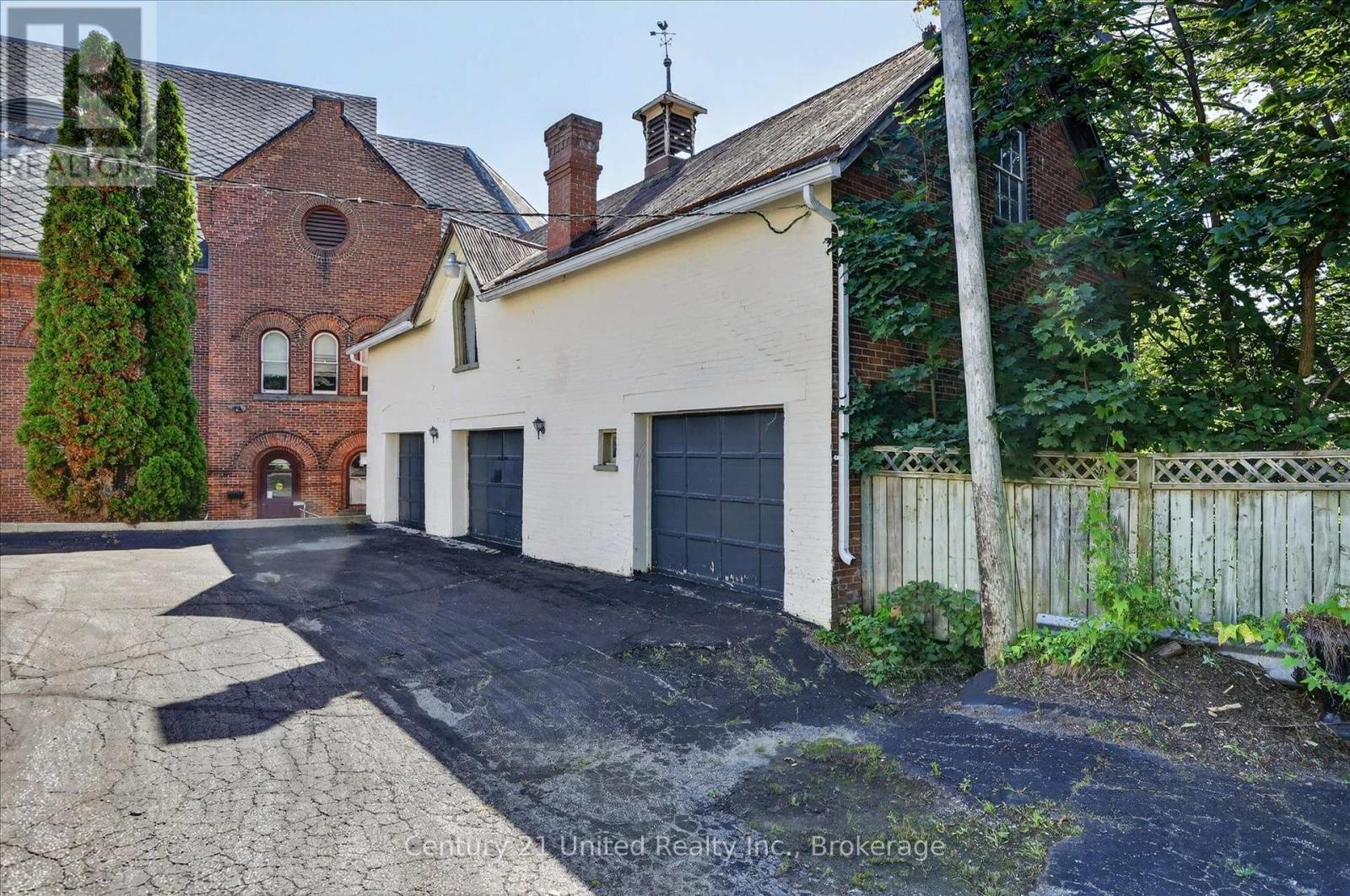 White brick garage with three dark doors beside a red-brick building and paved driveway.