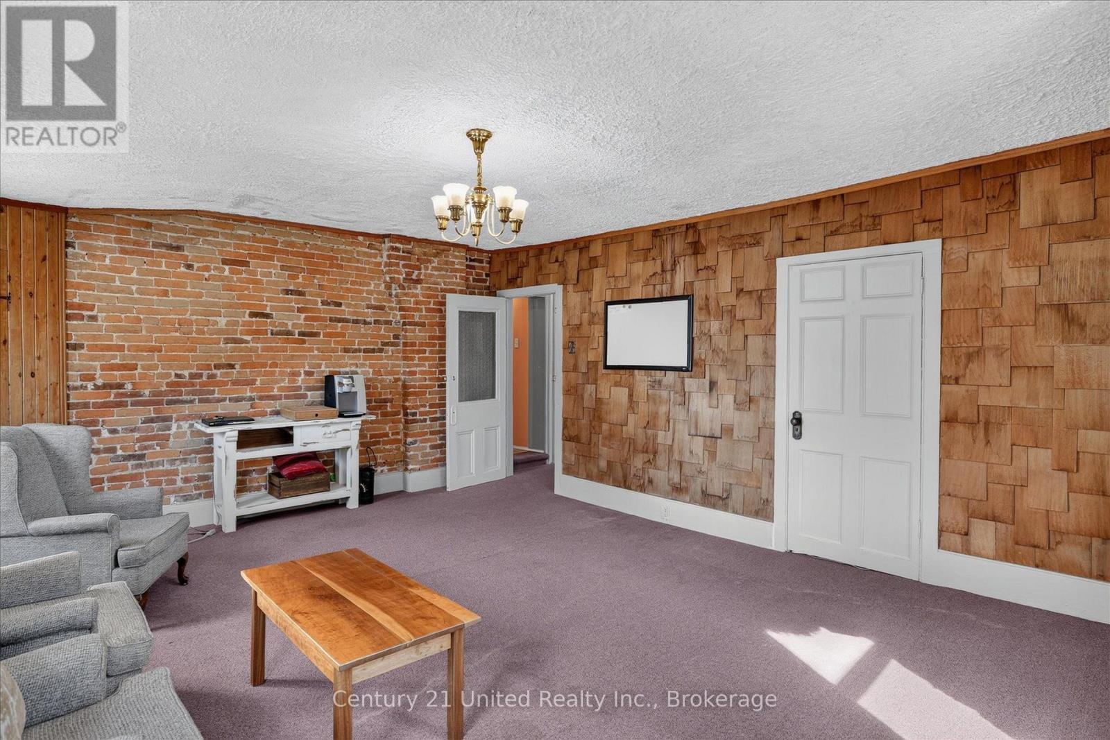 Living room with exposed brick, rustic wood-shingle walls, purple carpet, and gray seating.