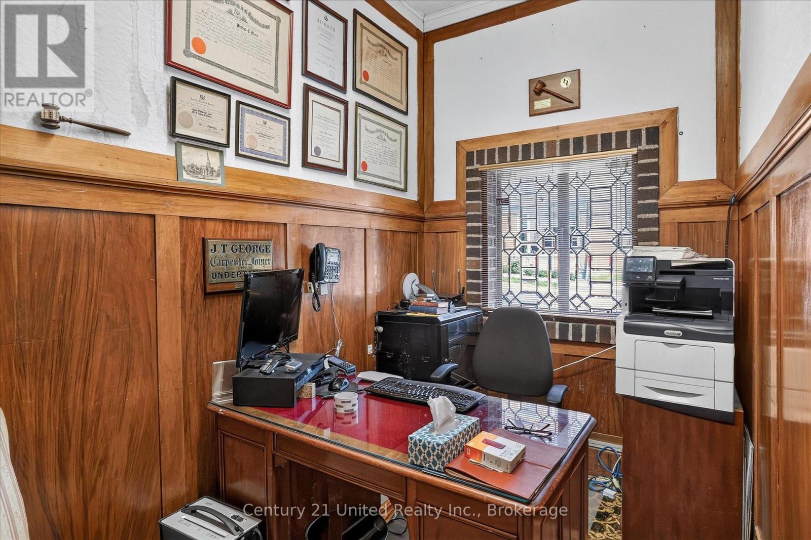 Wood-paneled office with a polished desk, computer, printer, and barred window.
