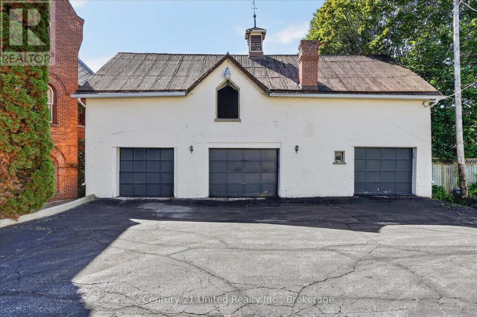 White brick garage with three dark doors and a weathered pitched roof beside a red brick building.