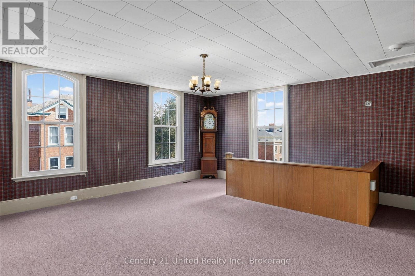 Spacious carpeted room with plaid walls, tall windows, a wood counter, and a grandfather clock.