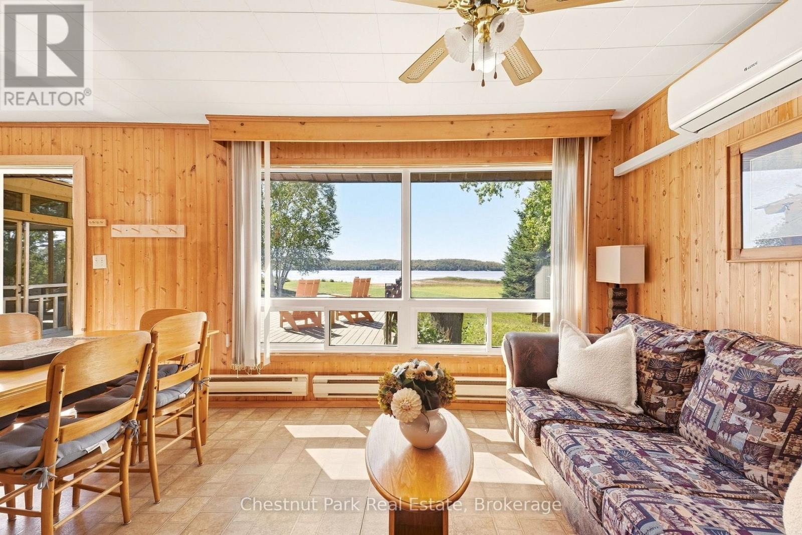 Furnished wood-paneled living and dining room with large windows overlooking a lake.