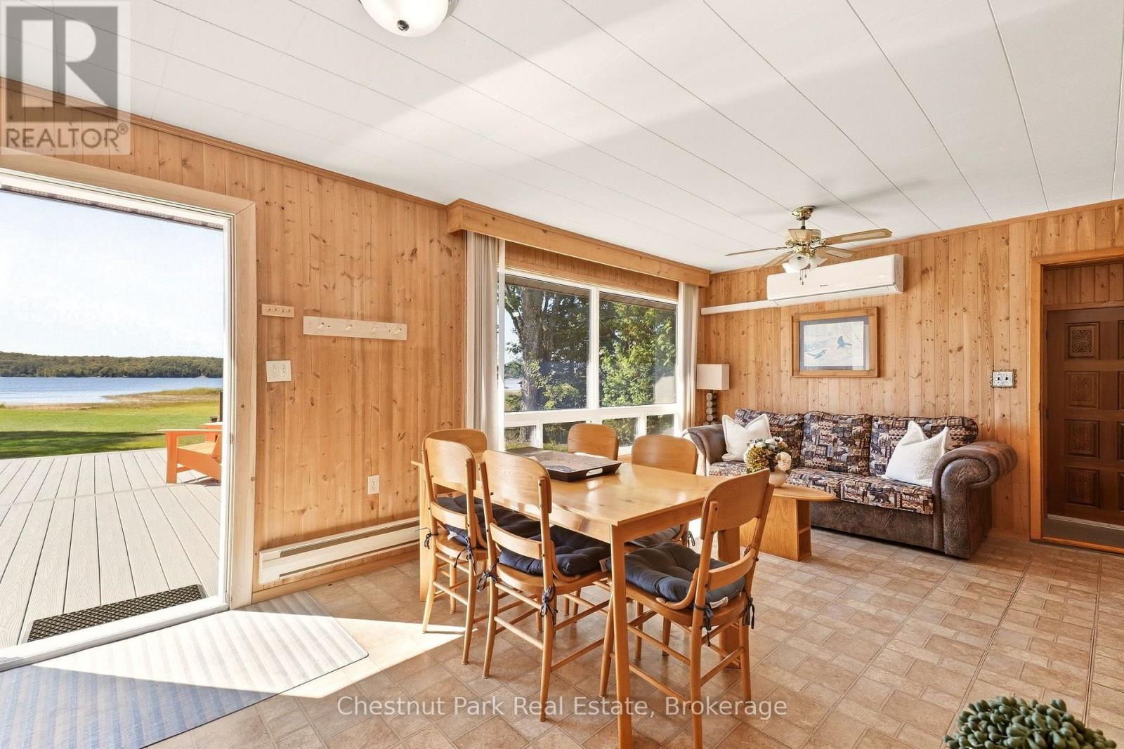 Cottage dining area with wood-paneled walls, a wooden table, and lake views through the open sliding doors.