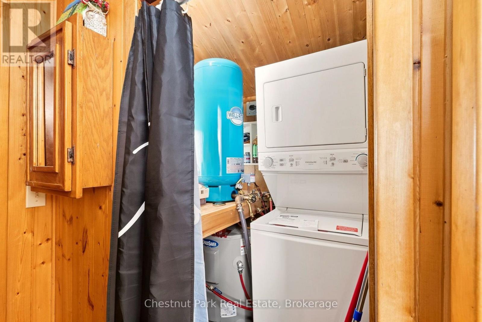 Utility area with stacked washer and dryer, blue pressure tank, and wood-paneled walls.