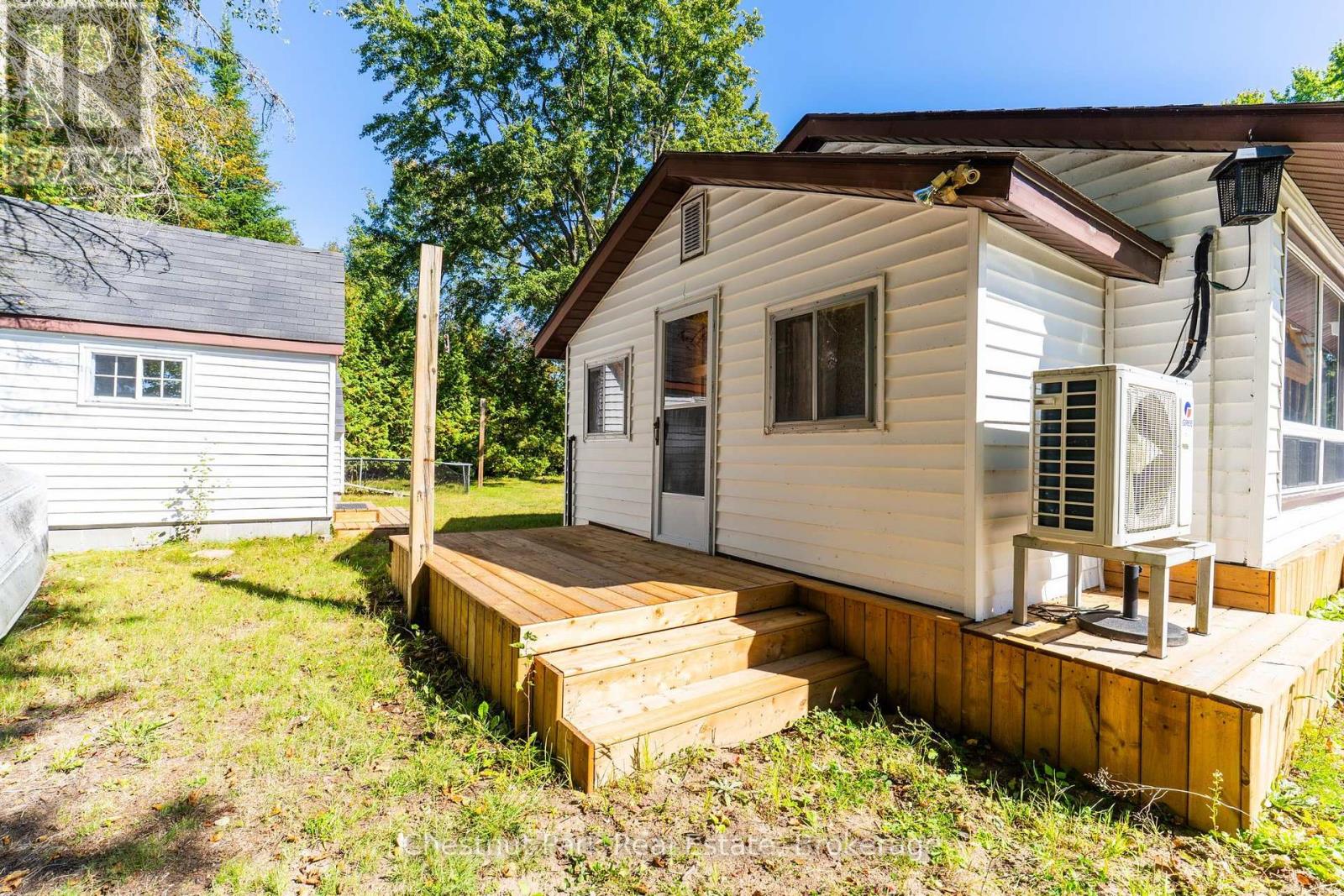 White cottage with a raised wooden deck and steps beside a small outbuilding.