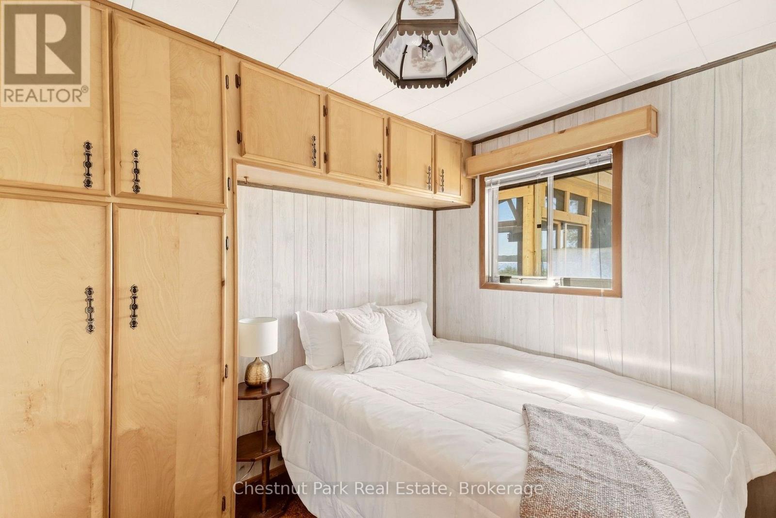Bedroom with a white bed, light-wood built-in cabinets, and a window overlooking water.
