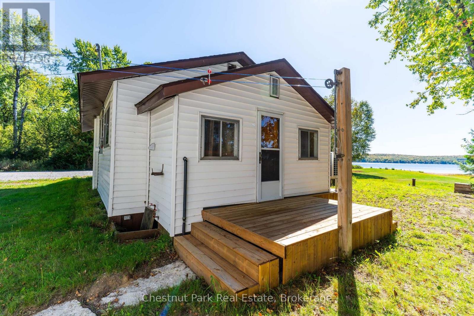 White cottage with a raised wooden deck overlooking a lake.