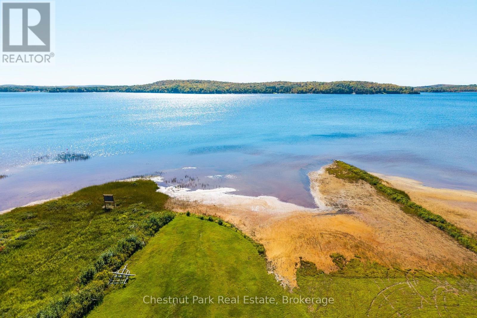 Aerial view of a grassy waterfront property with a sandy shore beside a broad lake.