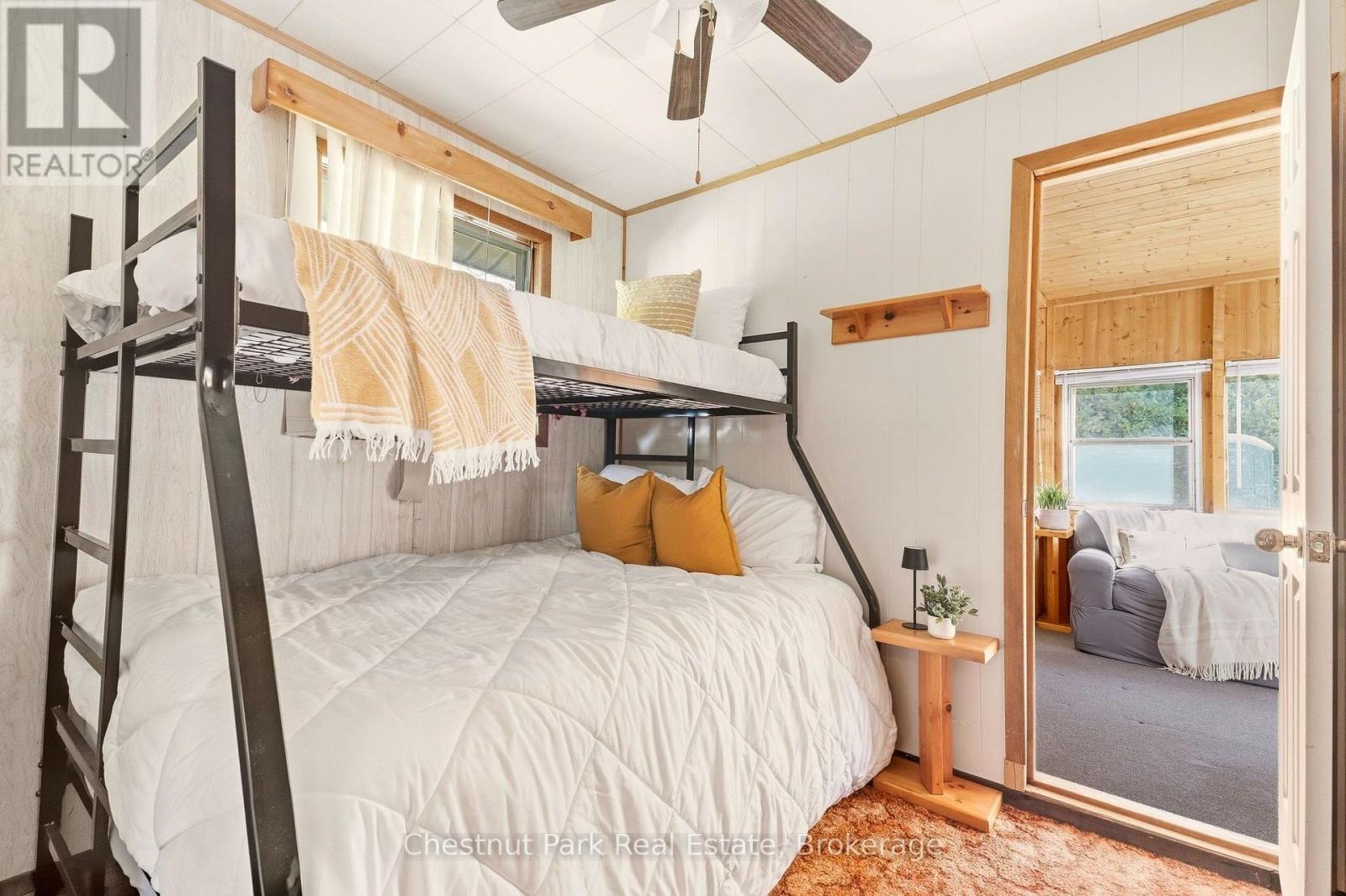 Bedroom with a black metal bunk bed, white bedding, and a doorway to a wood-paneled sitting room.