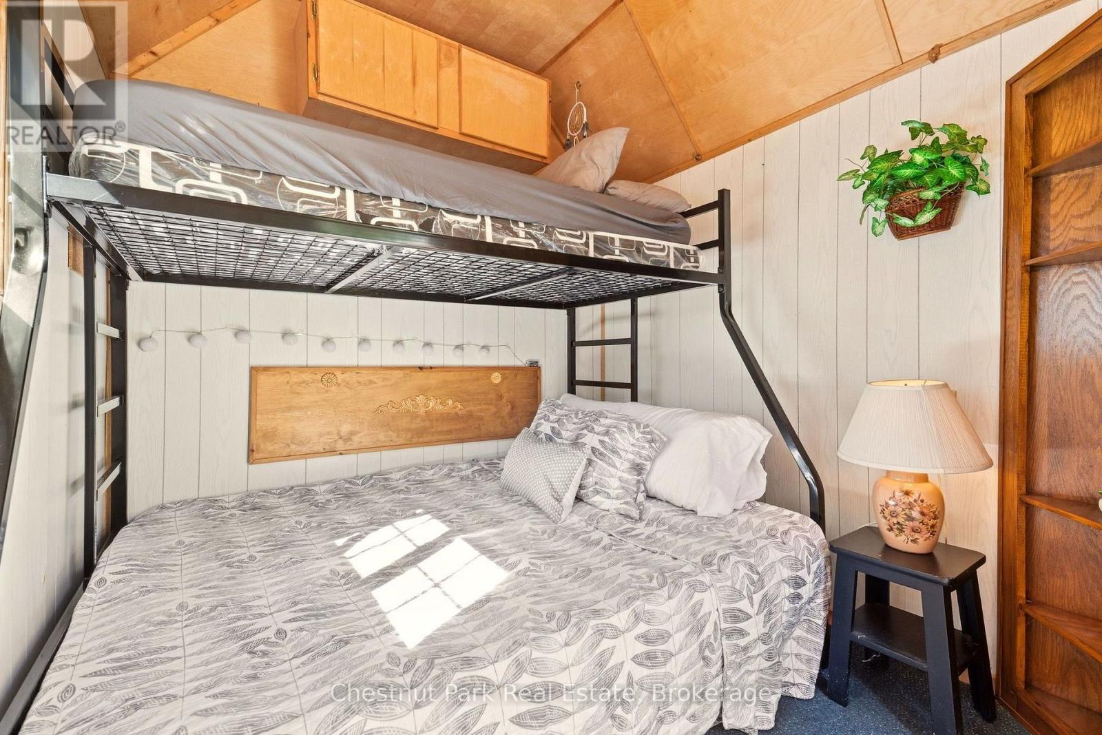 Bedroom with a gray-patterned bed beneath a black metal loft bunk and a sloped wood ceiling.