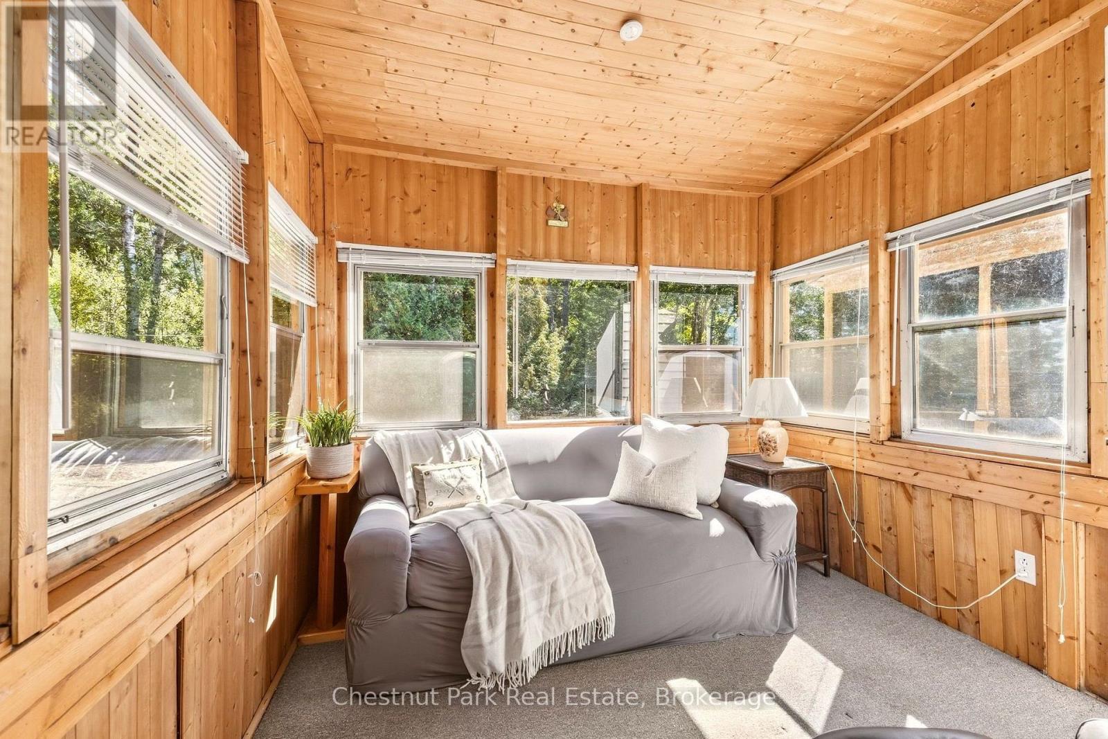 Wood-paneled sunroom with wraparound windows and a gray sofa draped with a white throw.