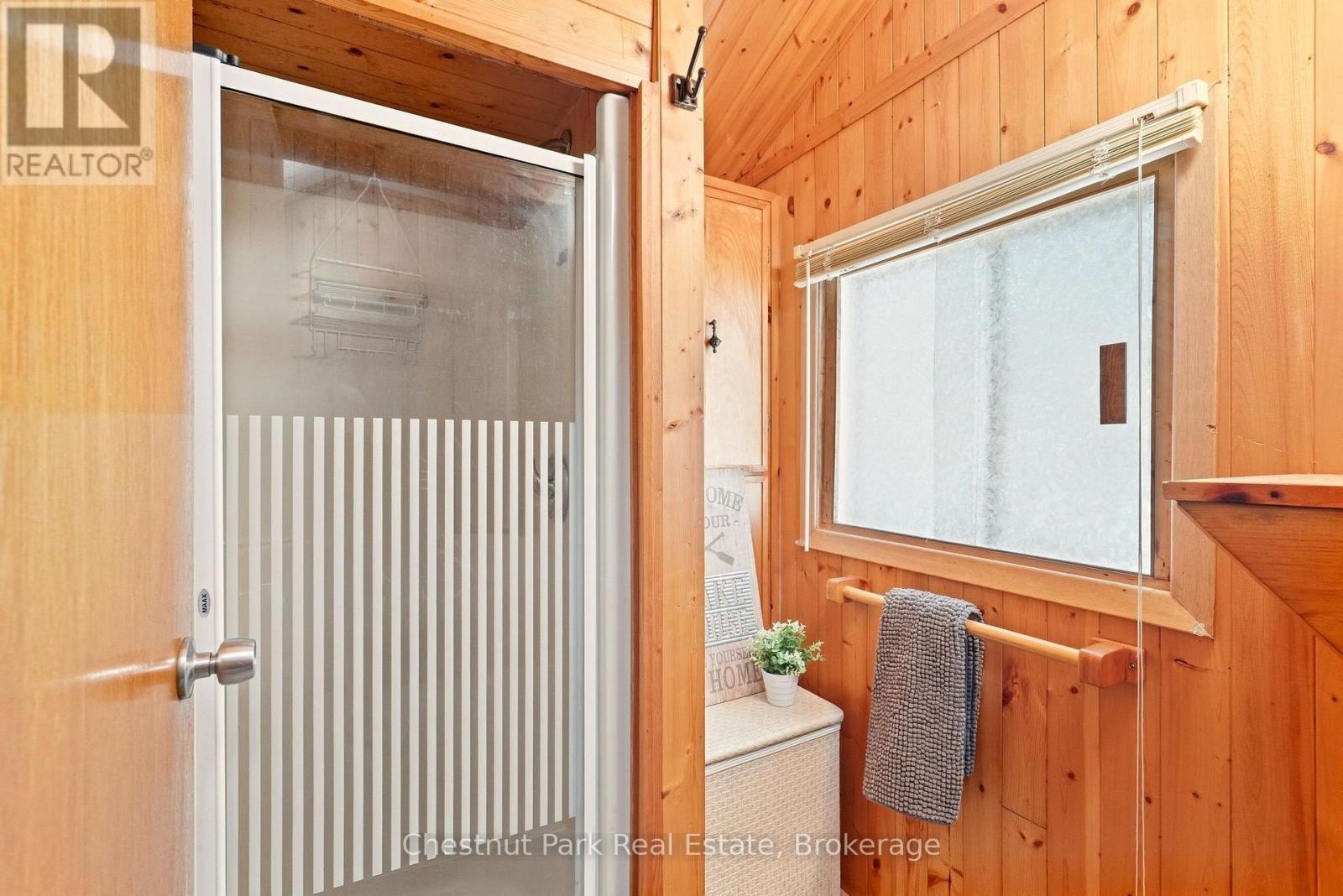 Wood-paneled bathroom with a striped glass shower enclosure, window, and towel rail.