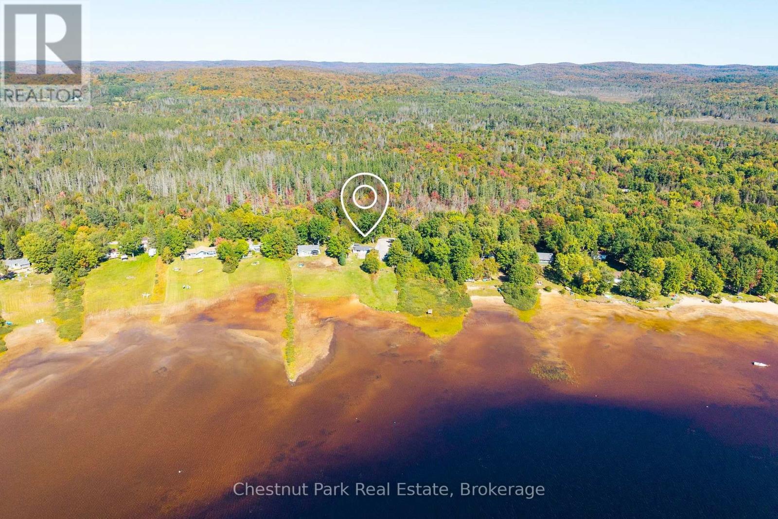Aerial view of a wooded lakefront property, marked by a pin among shoreline homes and autumn forest.