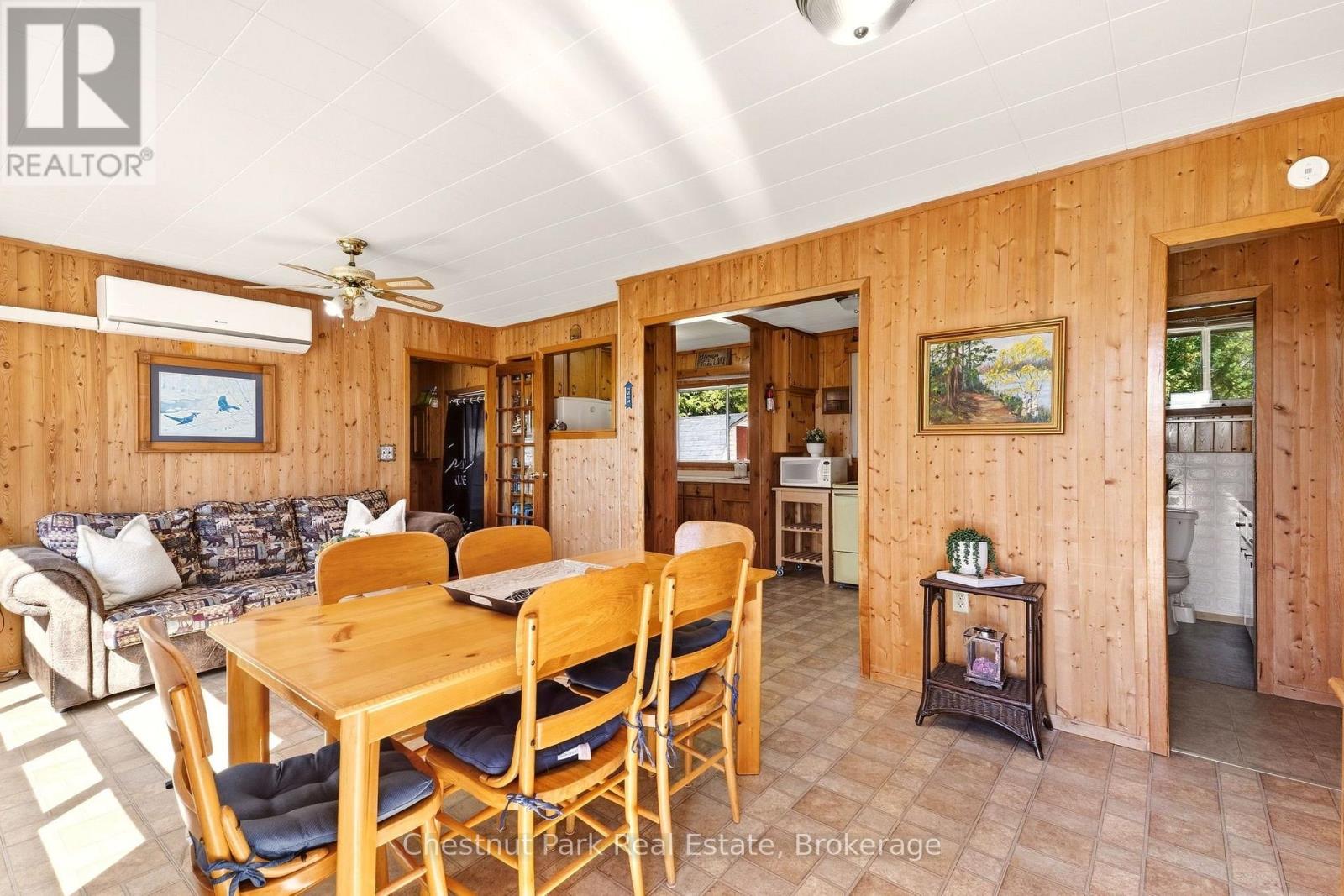 Dining and living area with wood-paneled walls, a wooden table, patterned sofa, and tiled floor.