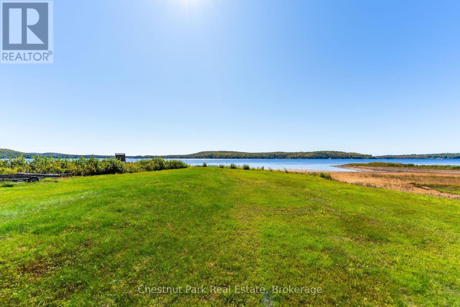 Waterfront lawn leading to a sandy lakeshore, with wooded hills across the water.