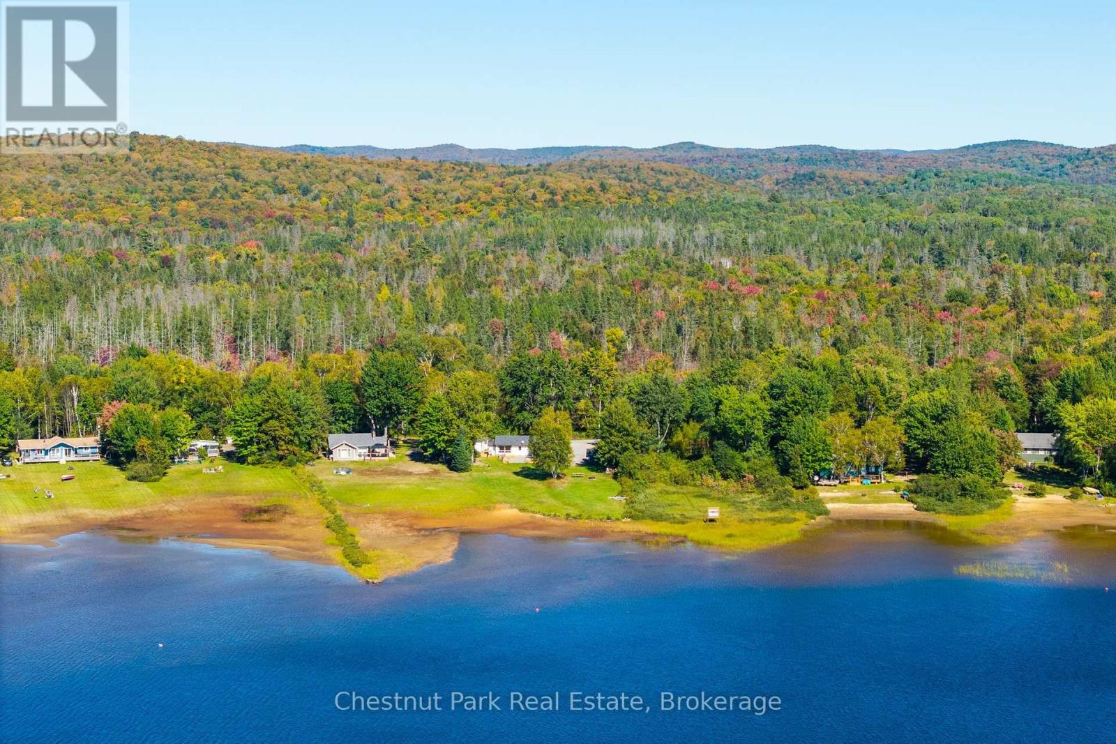Aerial lakefront view of cottages and grassy shoreline beneath autumn-colored wooded hills.