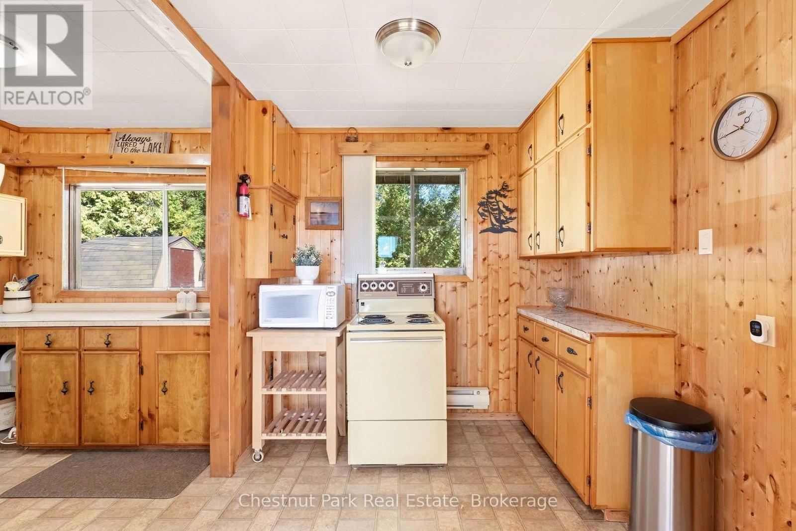 Wood-paneled kitchen with honey-colored cabinets, a white stove, and a microwave on a rolling shelf.
