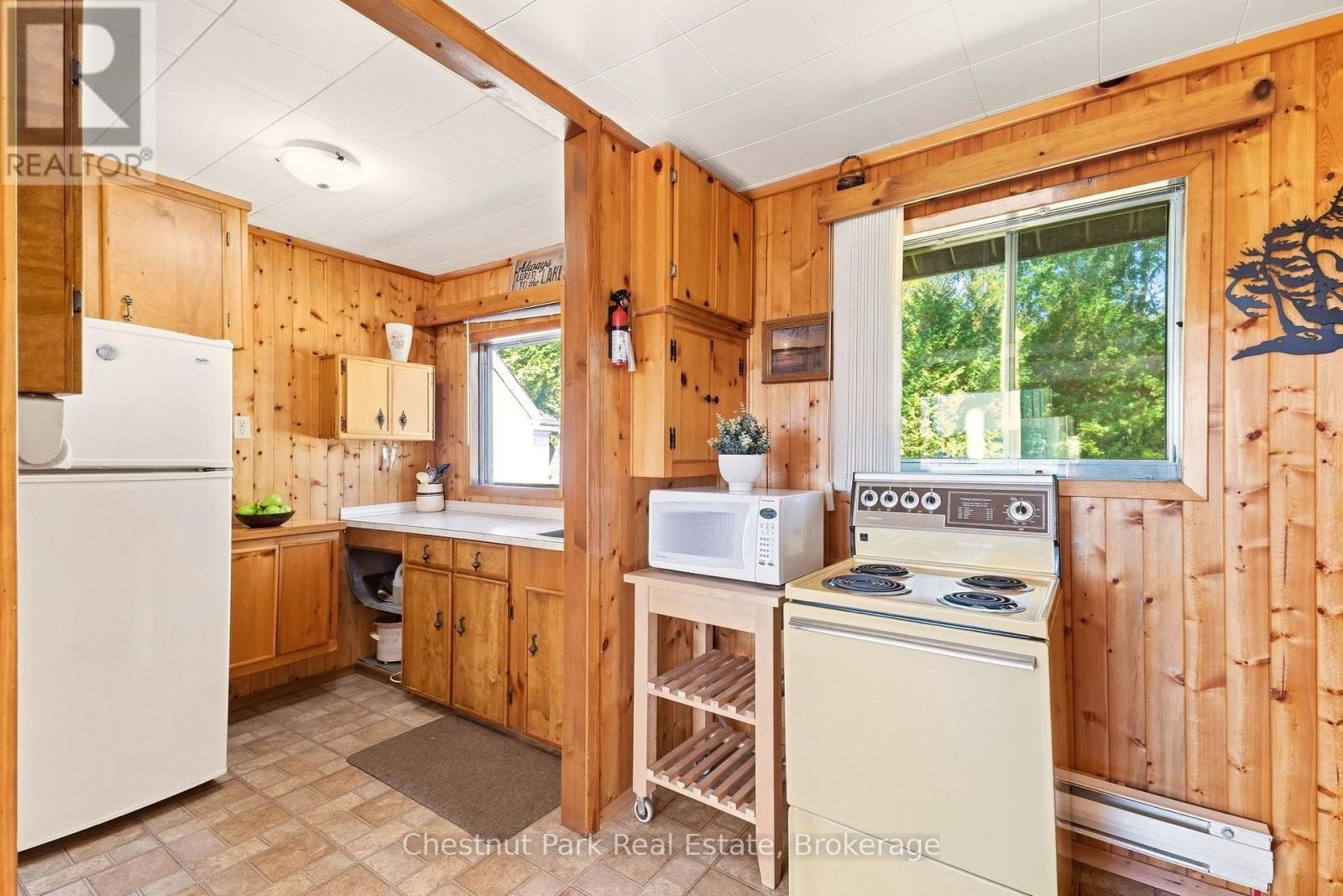 Cottage kitchen with knotty-pine cabinetry, a cream electric range, and windows overlooking trees.