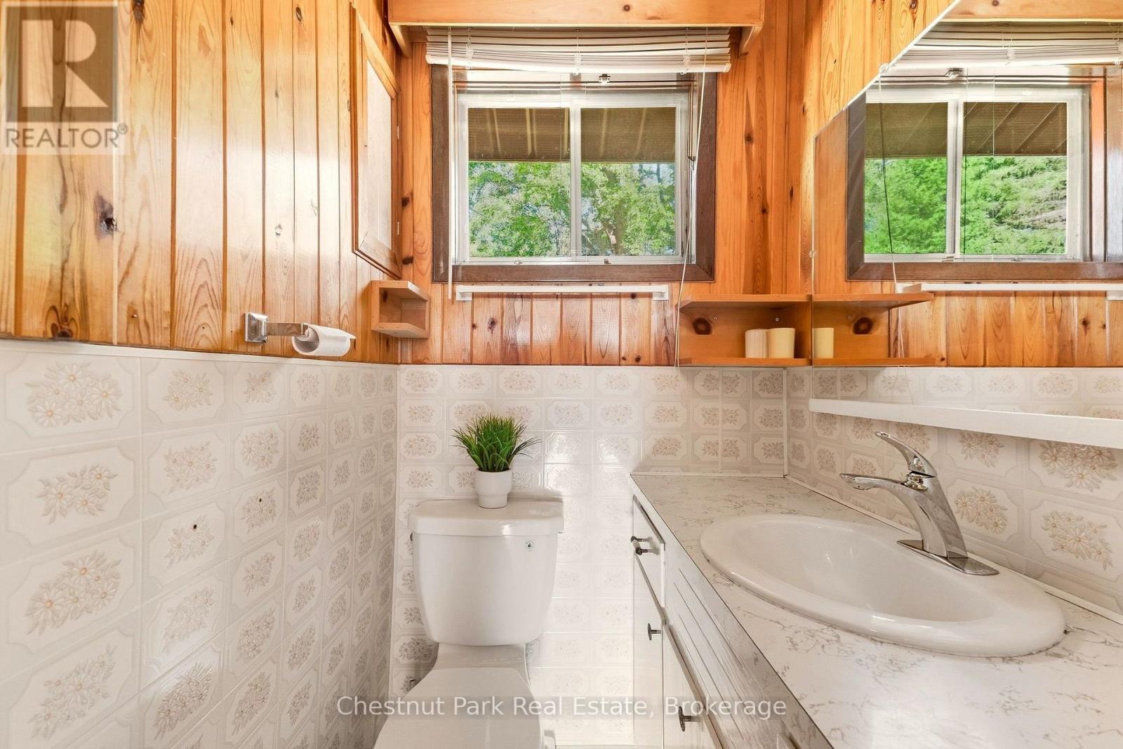 Bathroom with wood-paneled walls, floral tile, a toilet, and a long vanity with an oval sink.