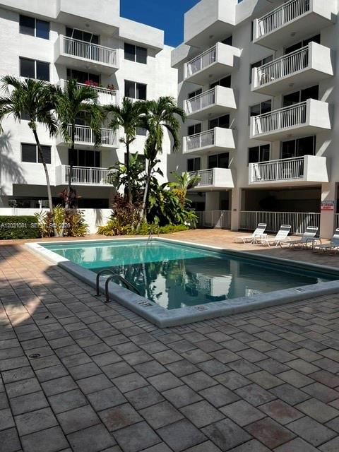 Condominium pool courtyard with palm trees, lounge chairs, and white balconies.