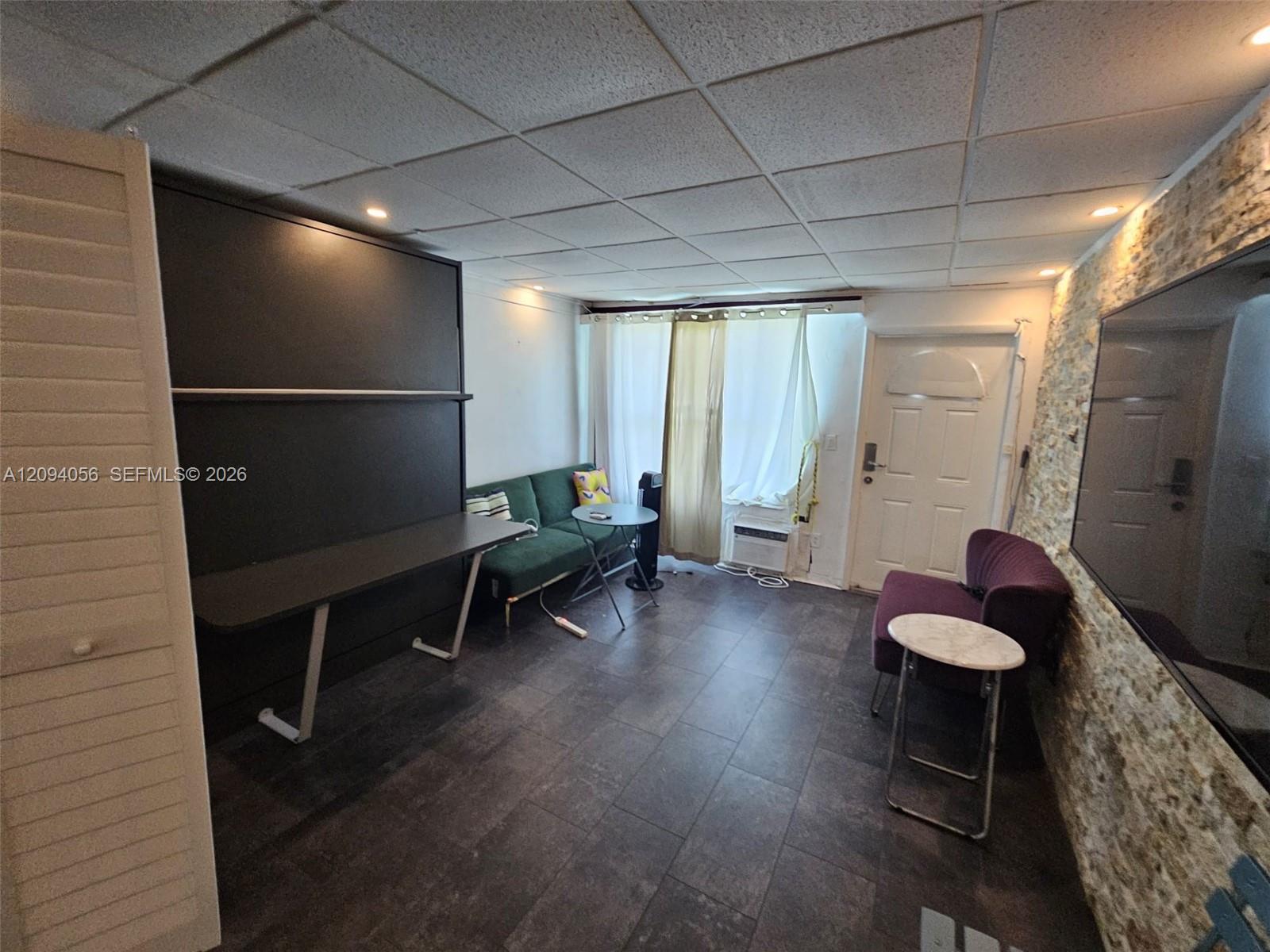 Furnished room with a built-in desk, green sofa, and television on a stone-textured wall.
