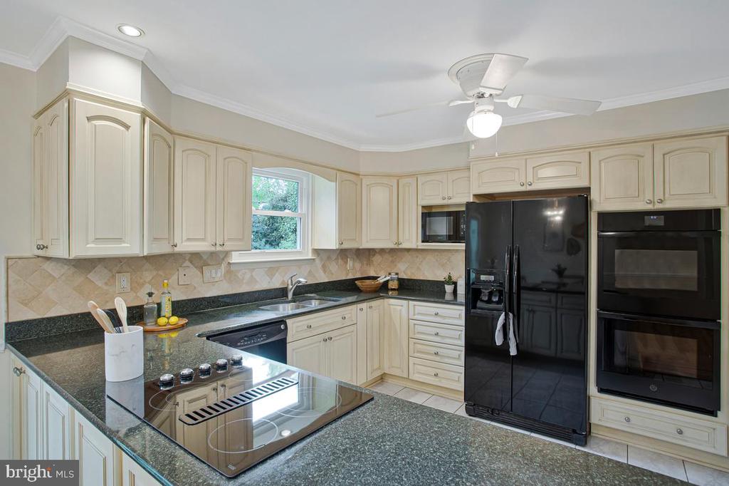 Kitchen with cream cabinets, dark granite counters, a peninsula cooktop, and black appliances.