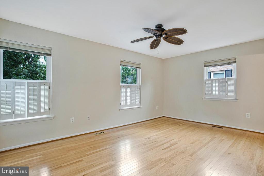 Empty room with hardwood floors, shuttered windows, and a ceiling fan.