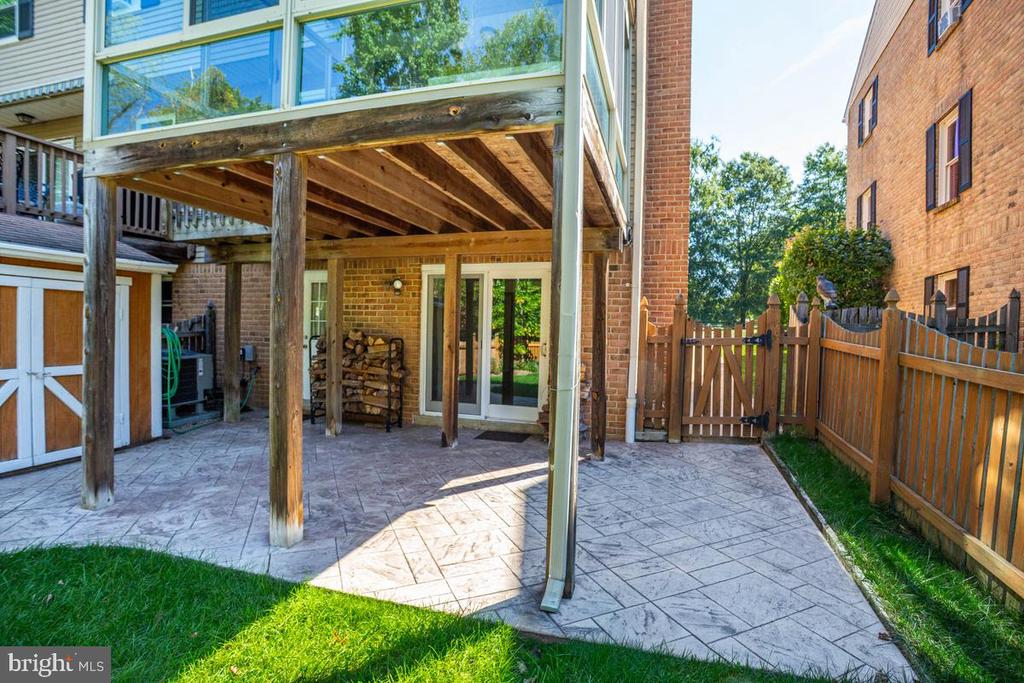 Townhouse patio with patterned paving beneath an elevated wooden deck and a wooden courtyard gate.