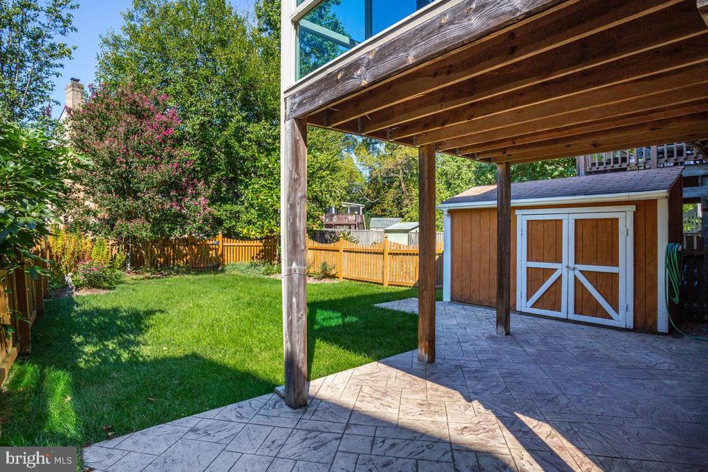 Covered backyard patio beside a fenced lawn and wooden storage shed.