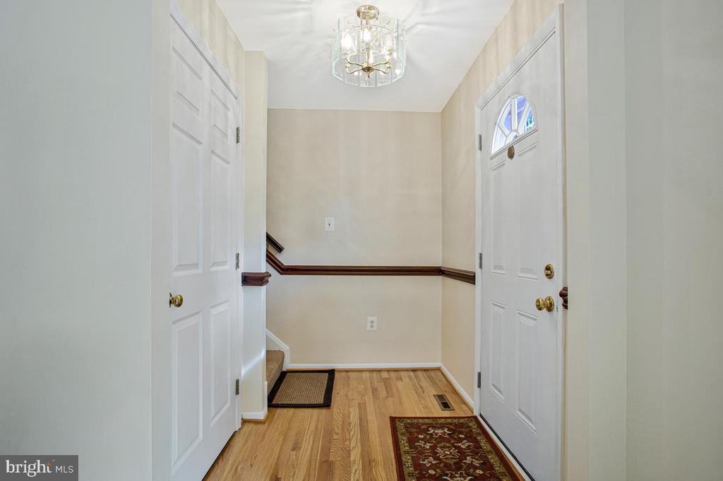 Entry foyer with hardwood floors, a white front door with arched glass, and a hanging chandelier.
