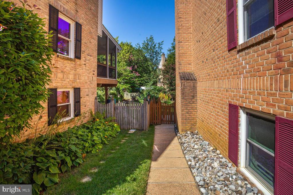 Brick residential courtyard with a walkway leading to a wooden gate, bordered by grass and shrubs.
