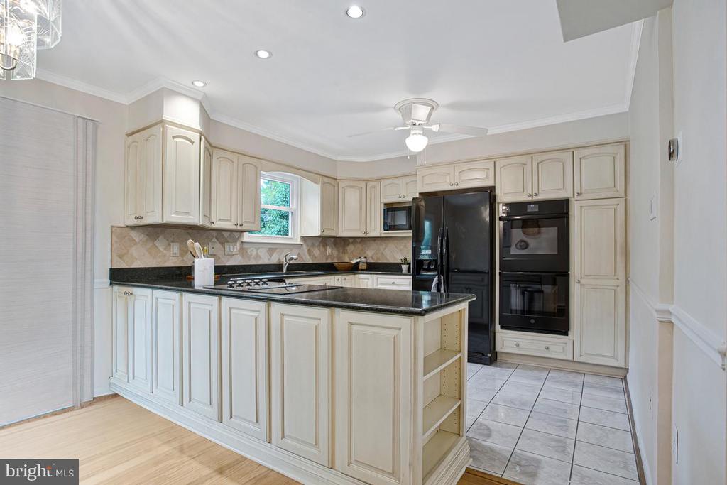 Kitchen with cream cabinetry, dark granite counters, a large peninsula, and black built-in appliances.