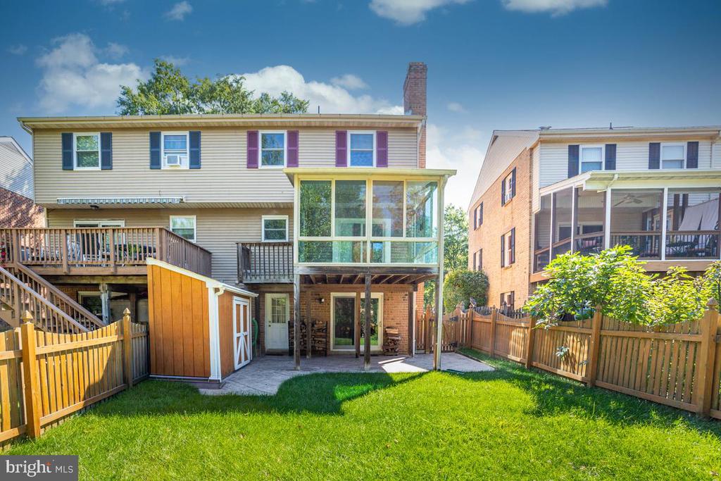 Rear of a two-story home with a raised deck, enclosed porch, shed, and fenced lawn.