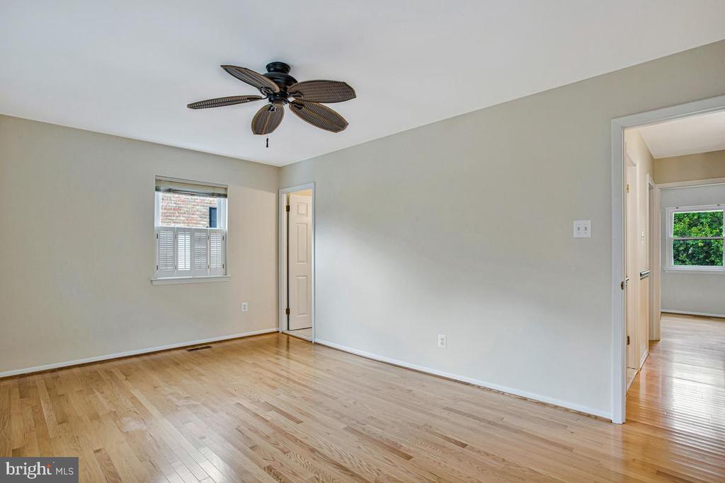Empty bedroom with hardwood floors, a dark ceiling fan, and a window with white shutters.