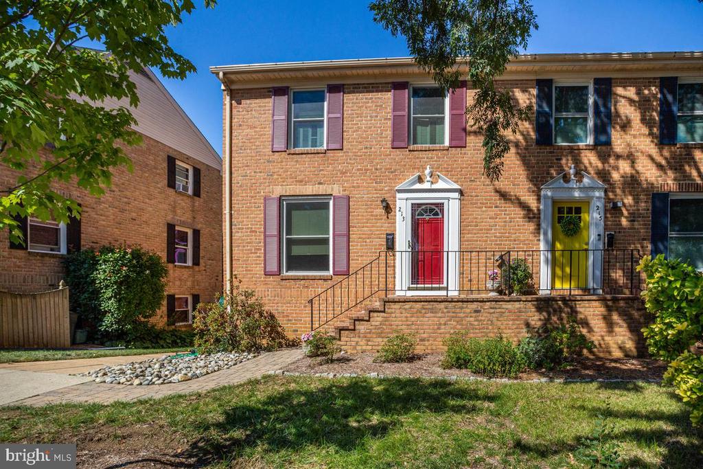 Brick townhouse with a red front door beside a neighboring yellow door and mature trees.