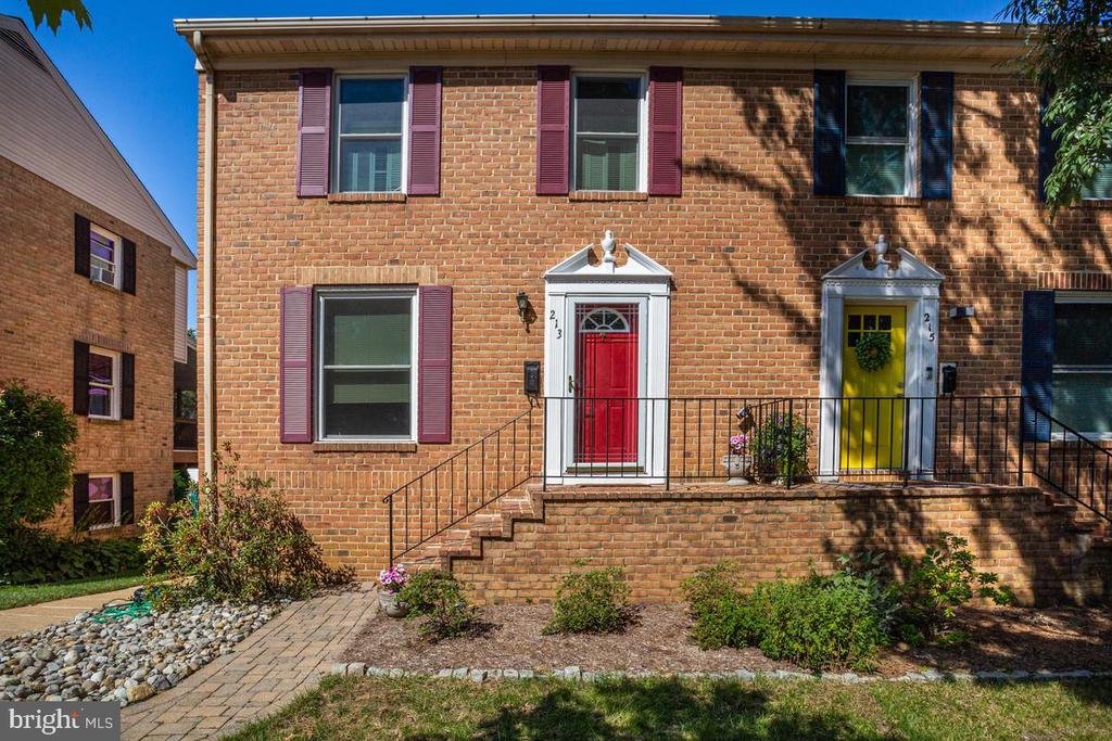 Brick townhouse with a red front door, burgundy shutters, and brick steps.