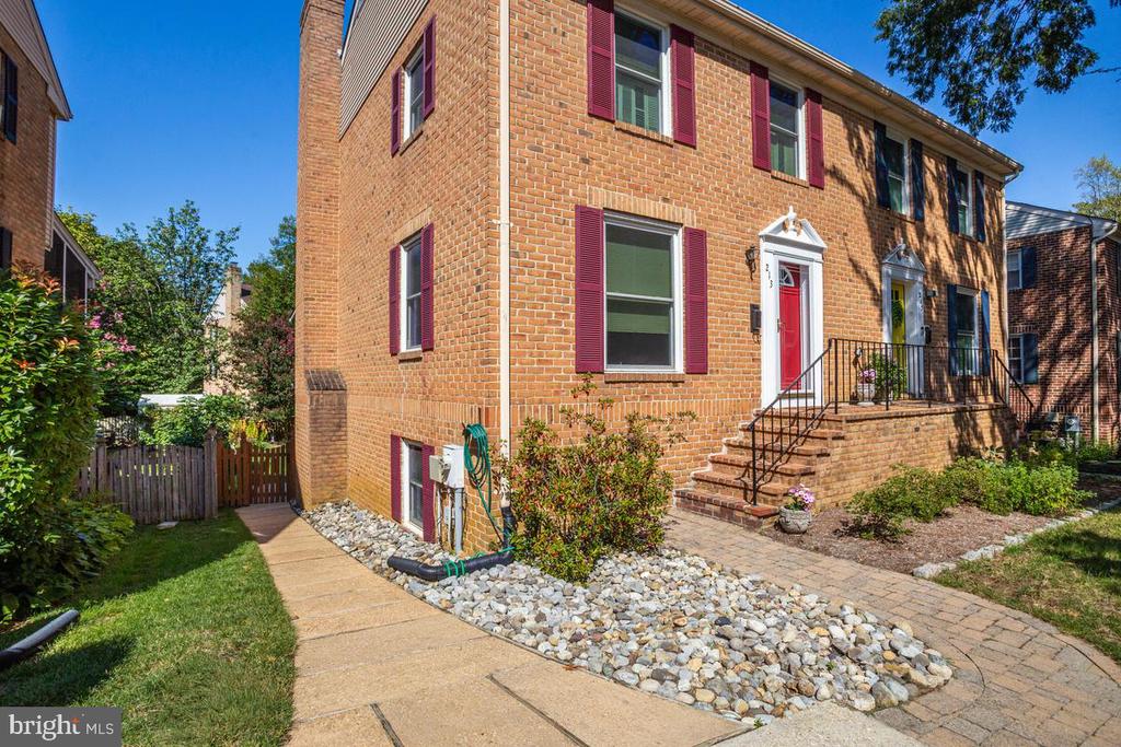 Brick townhouse with red shutters and doors, brick steps, and landscaped walkways.