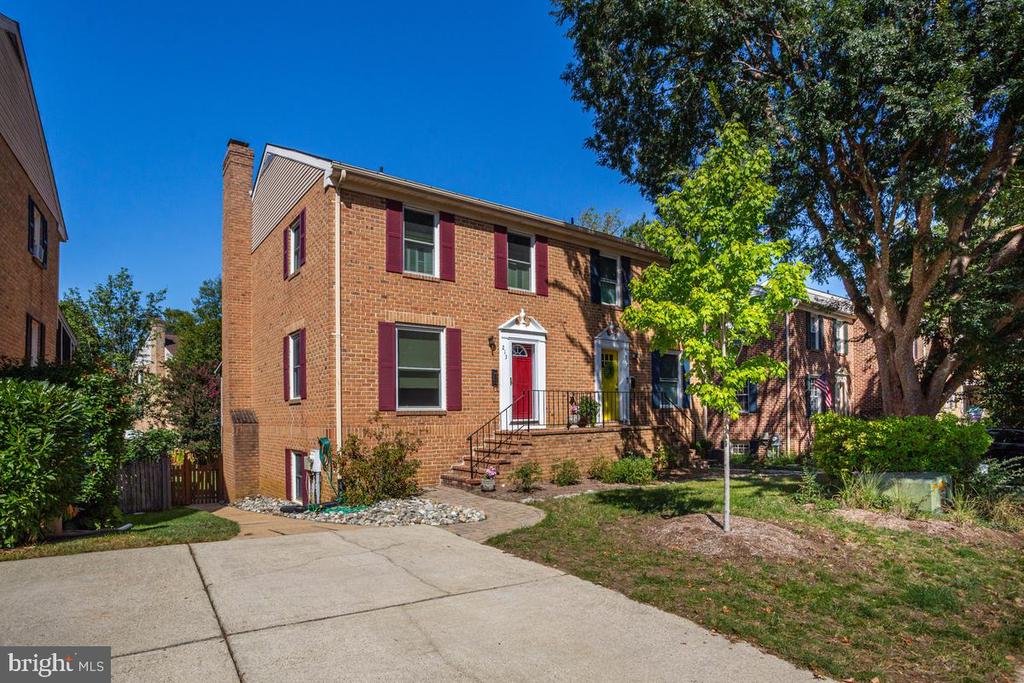 Two-story red brick townhouse with burgundy shutters, a red front door, and a concrete driveway.