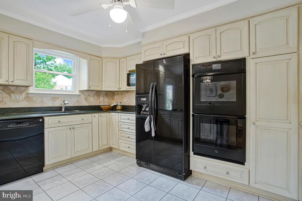 Kitchen with cream cabinets, dark countertops, black refrigerator, and built-in double oven.