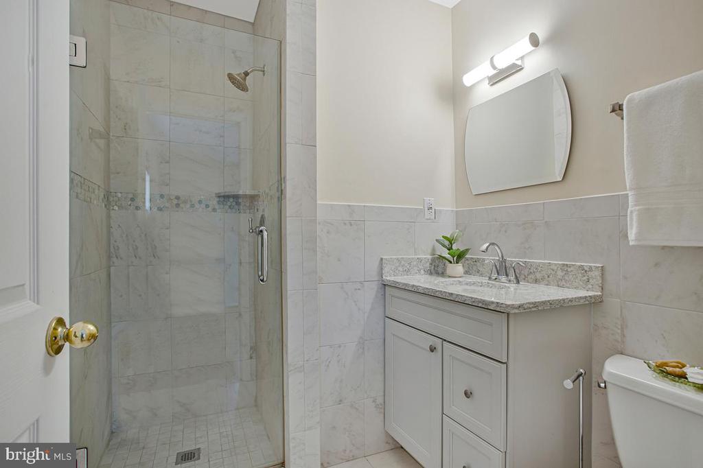 Bathroom with a glass shower, tiled walls, and white vanity with stone countertop.