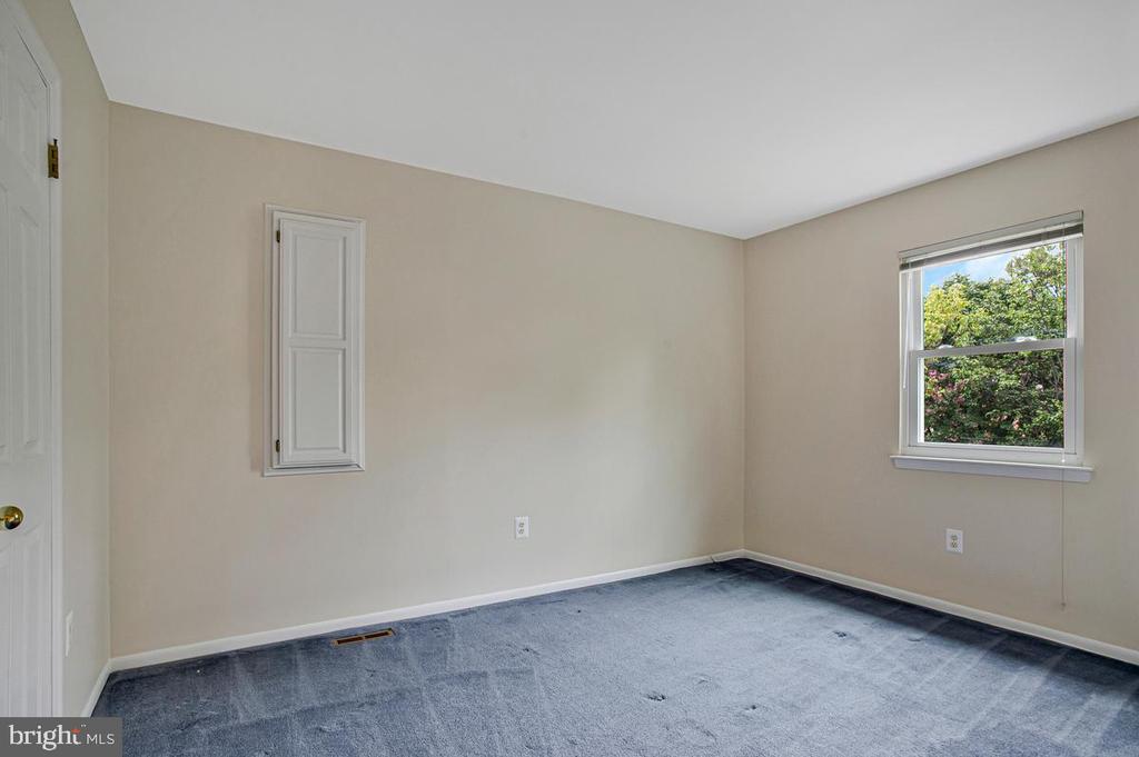 Empty bedroom with blue-gray carpet and a window overlooking leafy greenery.