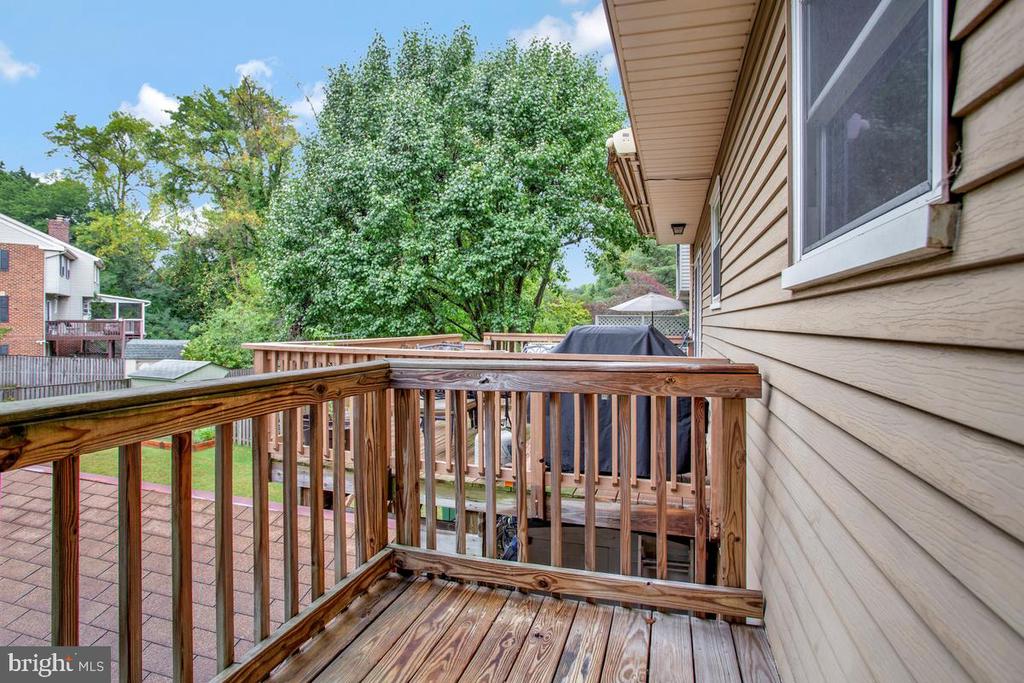 Wooden deck beside the home, with a covered grill and leafy trees beyond the railing.