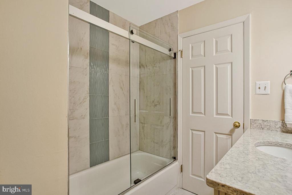 Bathroom with a glass-enclosed bathtub, marble-look tile, and granite vanity.