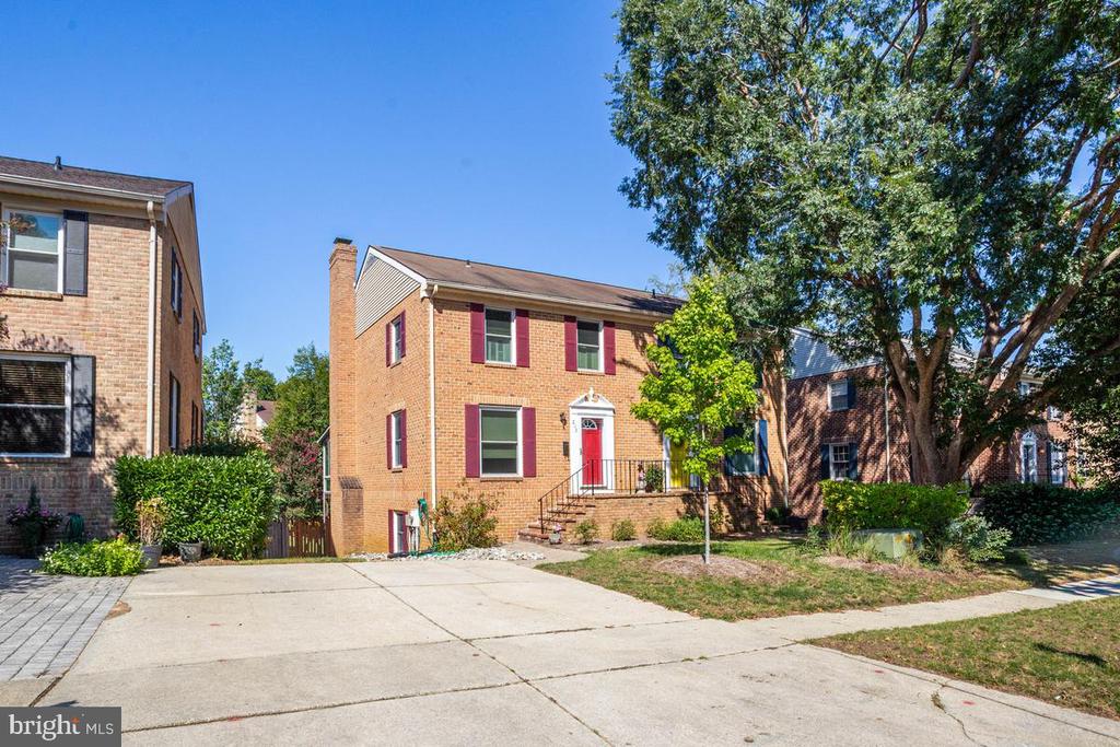 Two-story brick home with red shutters, a red front door, and a wide concrete driveway.