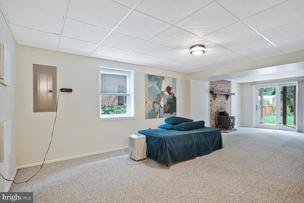 Carpeted lower-level living area with a brick fireplace, blue daybed and sliding glass doors to the garden.