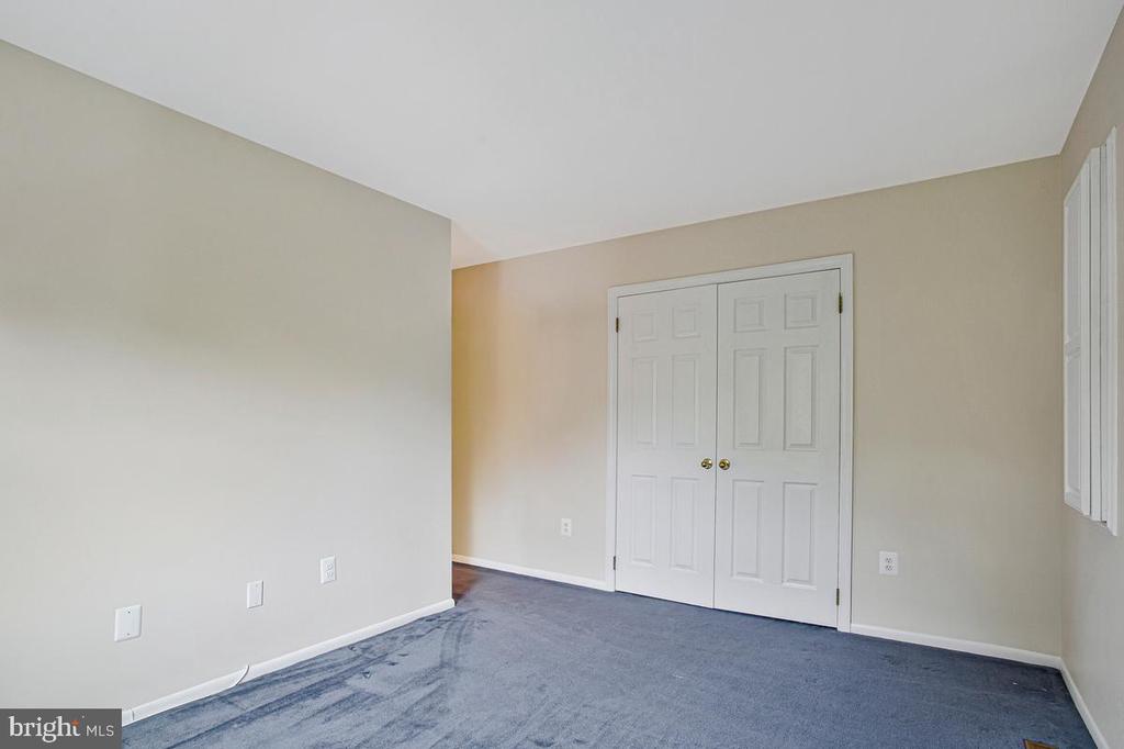 Empty bedroom with blue-gray carpet, white double closet doors, and a window with vertical blinds.