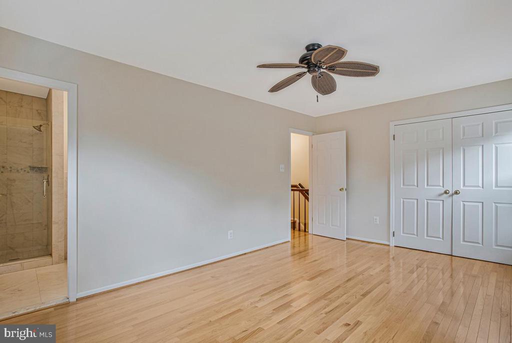 Unfurnished bedroom with hardwood floors, a ceiling fan, and white double closet doors.