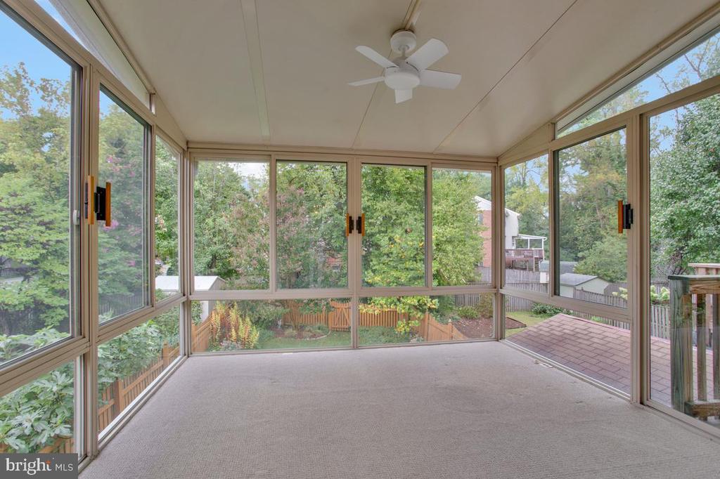 Sunroom with floor-to-ceiling windows overlooking a leafy fenced yard and patio.